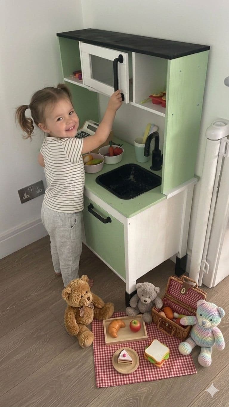 Smiling young girl with pigtails plays with a green toy kitchen and teddy bear picnic.
